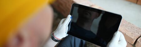 Close-up of smart guy's hands holding modern tablet in order to make workers construction process easier. Man using high-tech gadget and watching something on it. Copy space on screenの写真素材