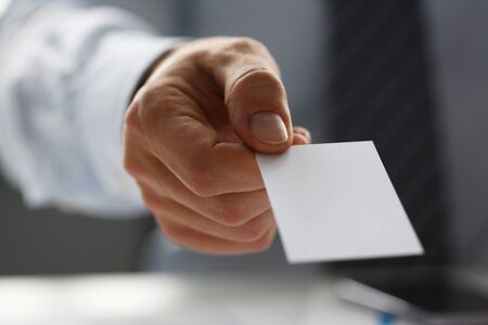 Male arm in suit give blank calling card to visitor closeup. White collar colleagues company name exchange job interview sale clerk id executive or ceo finance support formal identity conceptの写真素材