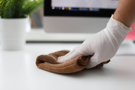 Male hand in white latex gloves wipes dust off table with brown microfiber. Cleaning service concept