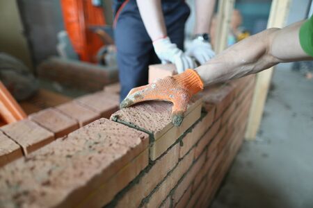 Close-up of big perfect masonry laid by skilled craftsman wearing protective outfit. Smart builder using special tools and equipment. Building conceptの写真素材