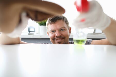 Smilind man hold in hand with white latex gloves wipes dust off table with brown microfiber....