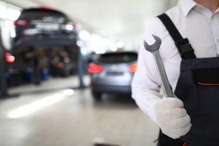 Serviceman in white protective gloves hold matall key in hand against car service station backgroundの写真素材