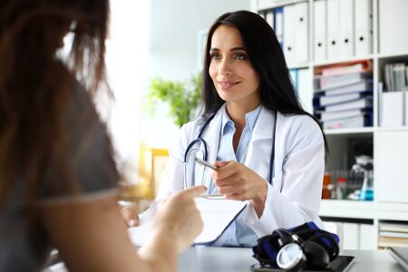 Beautiful smiling GP passing to patient silver pen asking to sign some paper documents portrait
