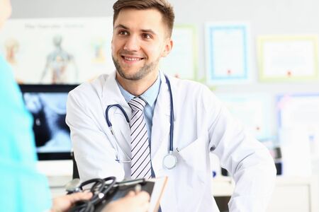 Portrait of smiling doctor in blue shirt and striped tie looking away with joy. Therapist in clinic cabinet and discussing therapy with colleague. Medical treatment conceptの写真素材