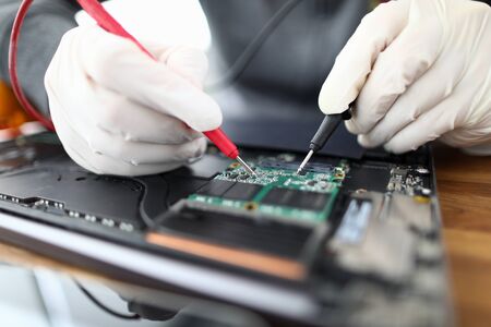 Male hands in white protective glove hold contact probe an electronic circuit tester. Laptop repair and technology conceptの写真素材