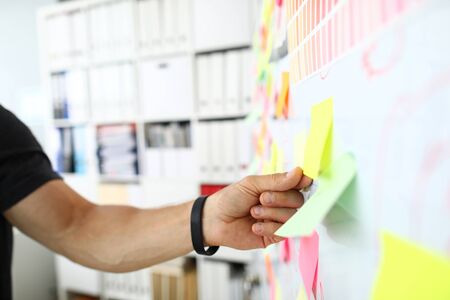 Male arm tearing away sticky paper note from whiteboard closeup