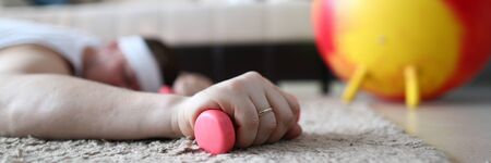 Tired Man Lying on Floor with Dumbbell in Hand. Strong Male Hand Holding Sports Equipment. Red...