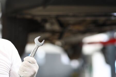 Focus on male specialist hand in white gloves holding important tool using for modern automobile underneath pipes repair. Machinery repairman concept. Blurred backgroundの写真素材