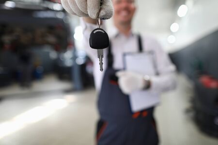 Focus on automechanic male hand holding automobile bunch of keys and important paper folder with information about fixed auto. Machinery checkup concept. Blurred backgroundの写真素材