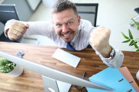 Top view of cheerful businessman standing near computer and looking at camera with happiness. Worker winning prize or signing profitable contract. Blurred backgroundの写真素材