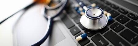 Stethoscope head with scattered tablets on a laptop keyboard backgroundの写真素材