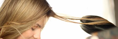 Blonde Woman Getting Hairstyle Closeup Photography. Iron Tool to Straight Hair. Styling Hairdo for Girl with Closed Eyes and Red Lips. Beautiful Female Model. Partial View Horizontal Photography.の写真素材