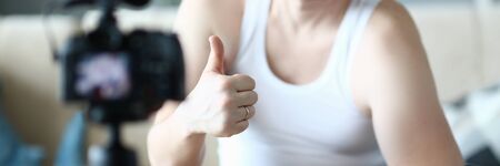 Happy Sportsman with Dumbbell Showing Thumb Up. Smiling Vlogger Recording Video with Exercise for Muscle on Digital Camera for Sport Vlog. Beard Man Practise Fitness in Apartment Partial View Photoの写真素材