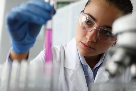 Female scientist in laboratory holds test tube with purple liquid in her hand. Human DNA research...