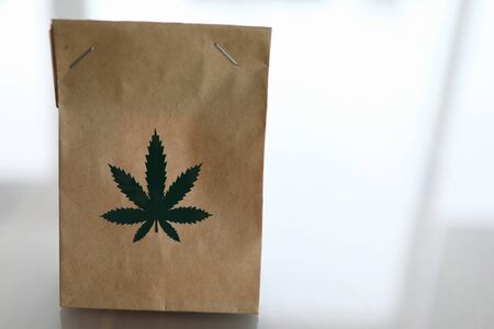 Bag of kraft brown paper with the marijuana logo lies on the table closeup backgroundの写真素材