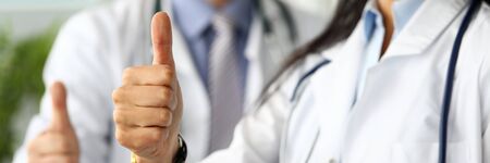 Group of doctors standing in row showing thumb up symbol as public opinion expression for good...