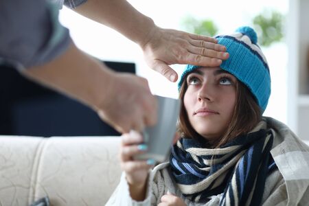 Portrait of beautiful lady sitting indoors and looking at someone touching forehead worn in warm hat...