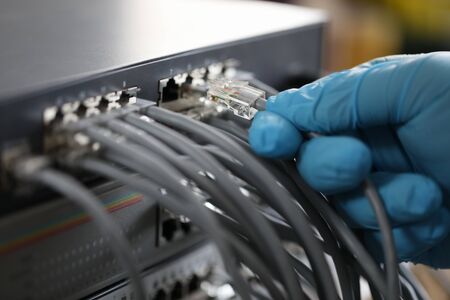 Focus on hand of hardworking man wearing blue glove and plugging high-tech wifi chords and cables used for right work of web router. Computer technology concept. Blurred backgroundの写真素材