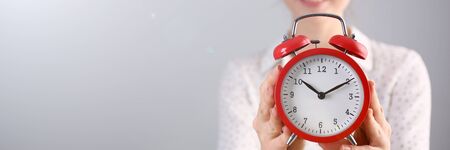 Focus on red alarm clock. Beautiful model in white blouse with curly brunette hair indicating on...