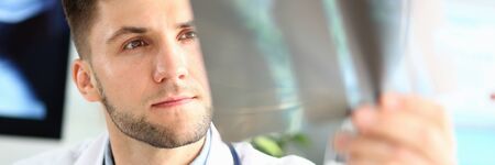 Portrait of thoughtful doc examining x-ray picture. Concentrated physician making diagnosis. Medical treatment and health care concept. Blurred backgroundの写真素材