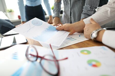 Manager holding in hand financial graph paper deliberating it with coworkers close-up