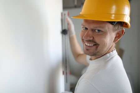 Portrait on handyman repairing wall. Man with measuring ruler or tool for making wall straight smiling at camera. Cheerful builder holding instrument in handsの写真素材