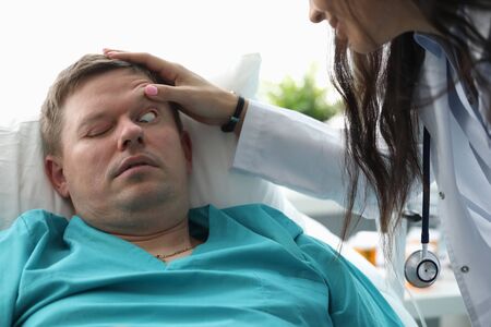 Close-up of ill patient lying in hospital ward. Professional doctor making eyeballs examination. Serious woman in medical gown. Healthcare and treatments conceptの写真素材
