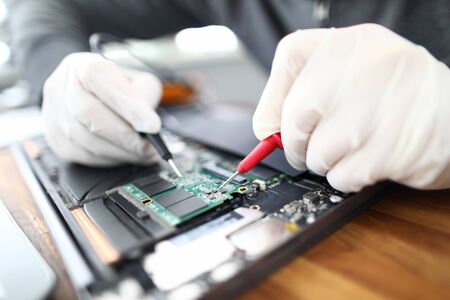 Close-up of circuit board in laptop. Technician soldering microchip using welding machine. Professional at computer service working on pc maintenance. Man in gloves fixing electronics and gadgetsの写真素材