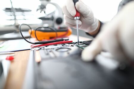 Close-up of technician male hands in gloves using screwdriver to fix laptop parts or install...