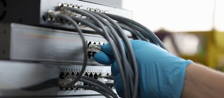 Focus on hand of hardworking man wearing blue glove and plugging high-tech wifi and cables used for...