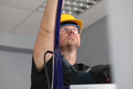 Portrait of handyman busy with tasks for apartment structure renewal and improvement of living space. Man climbing up on steps, wearing helmet and protective glassesの写真素材