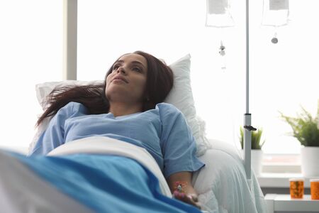 Portrait of wonderful sick woman lying in hospital ward in clinic. Beautiful businesswoman getting...