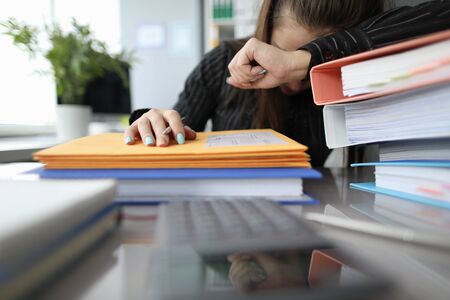 Close-up of stressed female feeling dizzy with workload. Lots of paperwork and problems at workplace. Colourful folders on desk. Job and business conceptの写真素材
