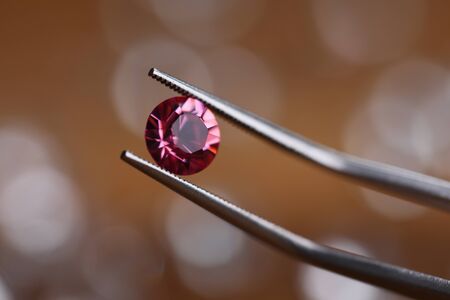 Jeweler in workshop holds pink stone in tweezers clamp closeup. Gemstone processing concept