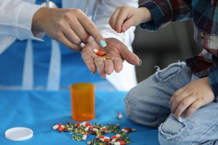 Focus on female hands with multicolored tablets. Pediatrician showing drugs to little kid. Family...