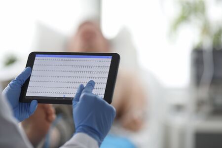 Focus on hands of female doctor touching screen of modern tablet with heart diagrams and examining...