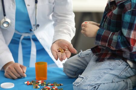 Focus on female hand holding multi colored pills, capsules and showing to little child. Smart professional pediatrician wearing white medical uniform. Healthcare and medicine conceptの写真素材