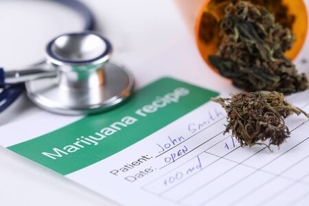 Close-up of marijuana recipe paper with dry trimmed cannabis on medical table. Doctors stethoscope tool for diagnostic. Healthcare and folk medicine conceptの写真素材