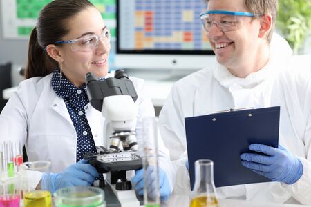 Portrait of smiling laboratory workers investigating biomaterial under black and white microscope....