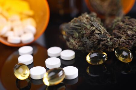 Close-up view of fish oil round capsules falling out of bottle. Dry marijuana and white pills on table. Medication and light narcotic for treatment. Healthcare conceptの写真素材