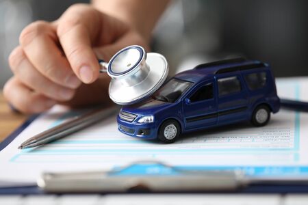 Close-up of male hand holding stethoscope and examining passenger car. Vehicle on important documents of insurance. Advertisement of service station conceptの写真素材