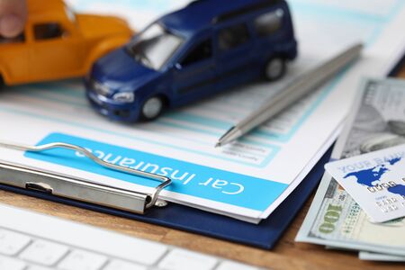 Close-up of important papers about car assurance. Credit bank card and currency money lying on table. Blue and orange toy cars on folder. Advertisement and business conceptの写真素材