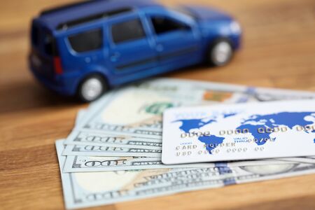 Close-up of bank credit card and money cash lying on table. Blue toy passenger machine and dollar banknotes. Finance car assurance and business conceptの写真素材
