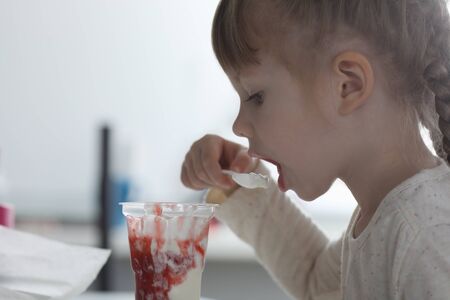 Portrait of child eating with spoon sweet ice-cream with berry jam. Small kid sitting at table and...