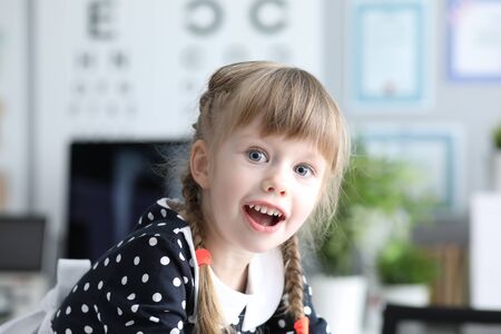 Portrait of positive child in polka-dot dress looking at camera with interest. Surprised girl visiting ophthalmologist. Medicine and healthy lifestyleの写真素材