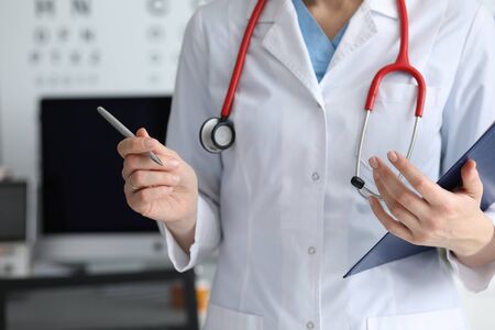 Close-up of female doctor in white medical gown and stethoscope holding paper folder with important documents and pen. Medicine and healthcare conceptの写真素材