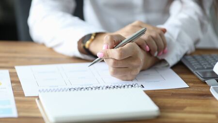 Close-up view of womans hands filling paper with months. Person sitting in office with silver pen...