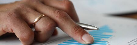 Focus on male hands holding metallic ball pen and pointing at important graphs of statistics data. Financial forecast of new start-up. Stock Exchange, Securities Market concept. Blurred backgroundの写真素材