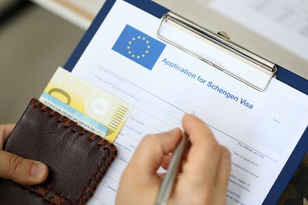 Top view of man filling out documents for Schengen visa while holding money. Travel conceptの写真素材