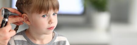 Portrait of smart child sitting in modern clinic office and looking away with sadness. Professional...